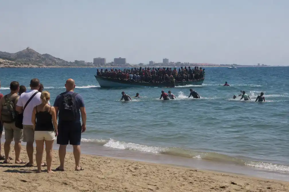 Migranten springen van overvolle boot en zwemmen naar Spaans strand; toeristen vluchten